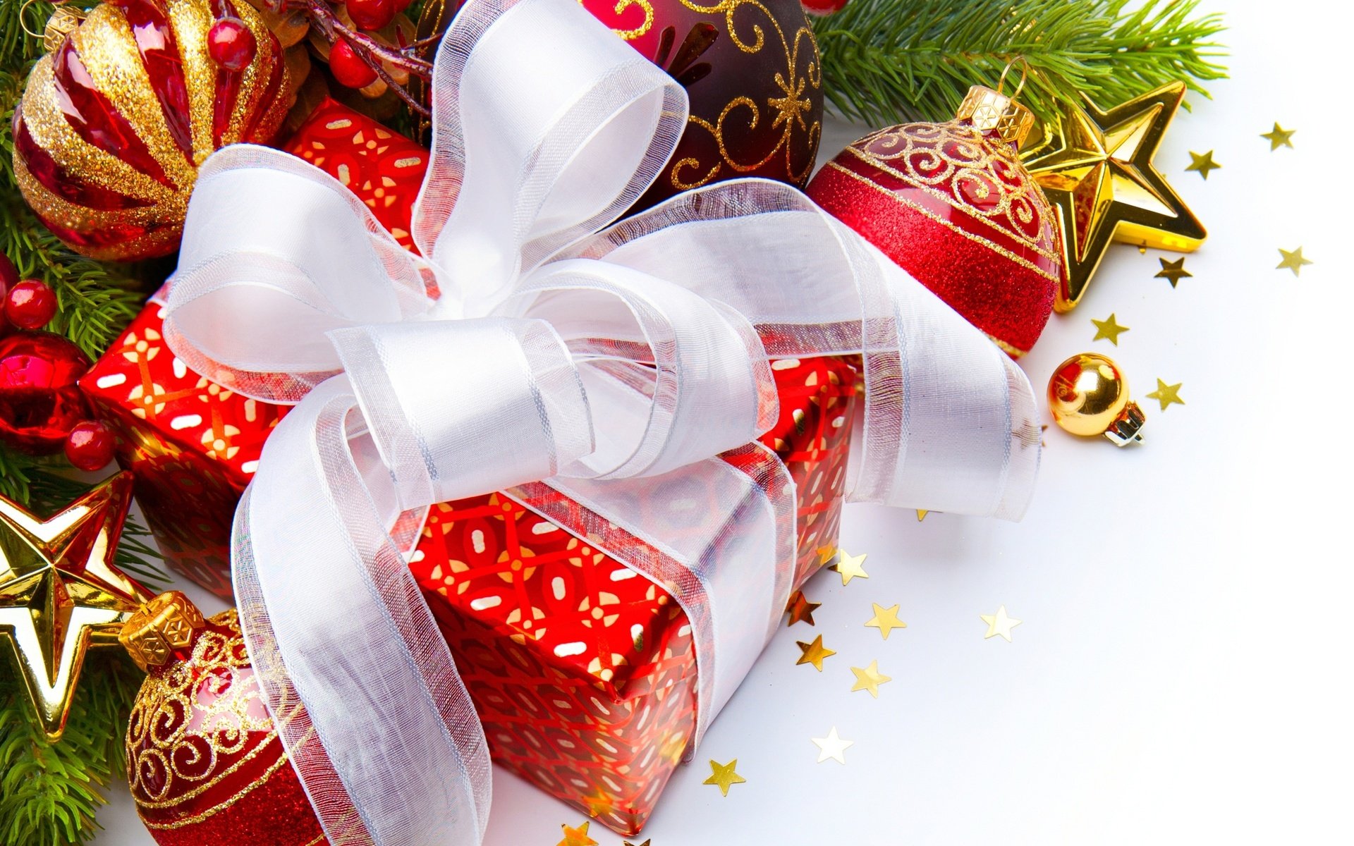 A vibrant HD desktop wallpaper featuring a festive Christmas gift wrapped with a white ribbon, surrounded by colorful holiday ornaments and green pine branches.