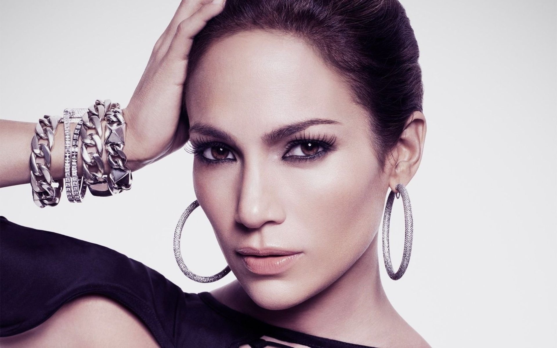 HD PC desktop wallpaper: close-up portrait of an unidentified female celebrity with sleek hair, smoky eyes, large hoop earrings and stacked bracelets against a pale backdrop.