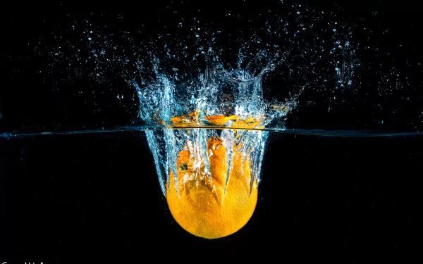 A vibrant orange fruit splashes into water, creating dynamic splashes against a dark background. This HD wallpaper captures the refreshing essence of food and color.