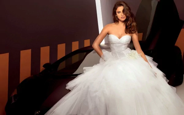 Irina Shayk poses elegantly in a stunning white gown against a sleek black car, creating a captivating HD wallpaper and background for fans of celebrity imagery.