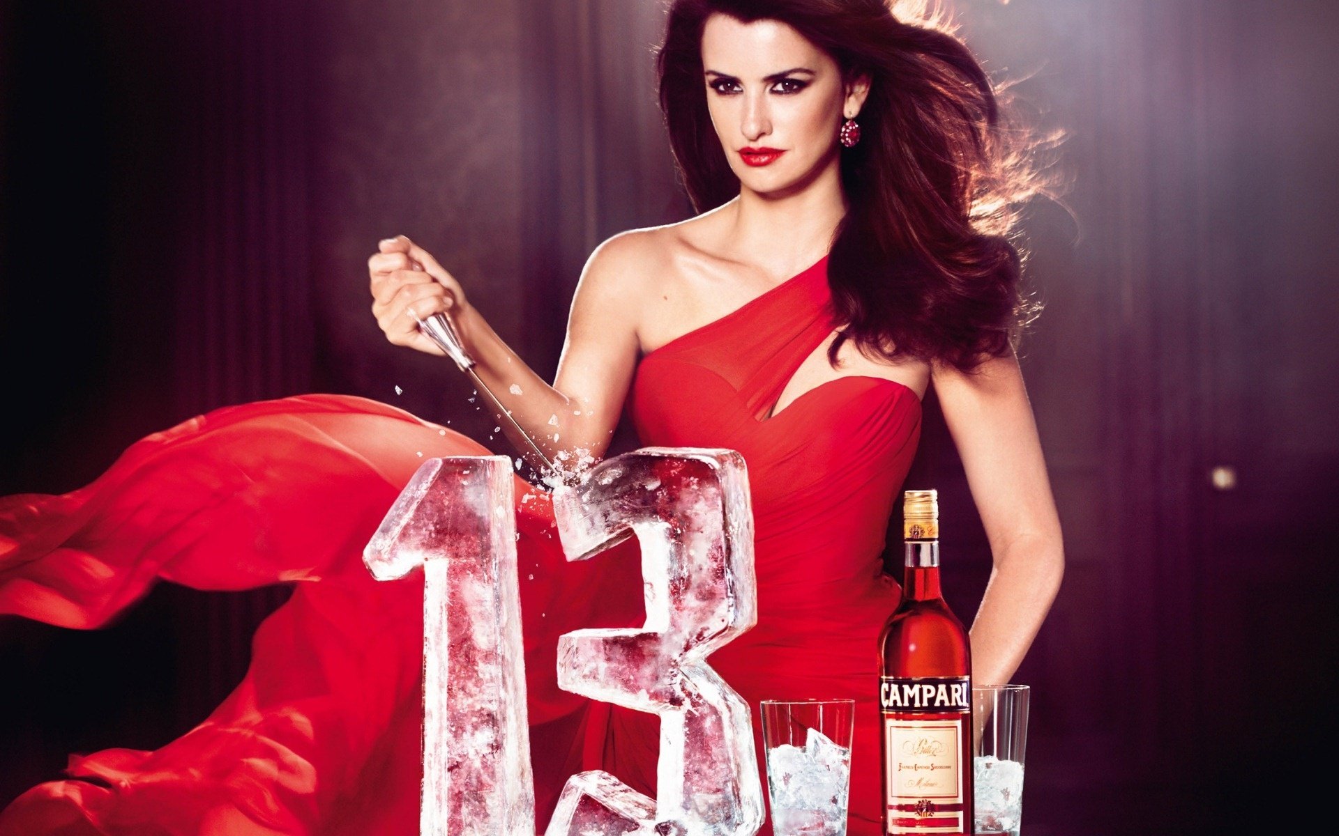 HD desktop wallpaper featuring celebrity Penelope Cruz in a flowing red dress standing beside a large ice sculpture of the number 13 with a bottle of Campari.