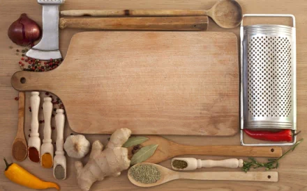 HD PC desktop wallpaper featuring an assortment of herbs, spices, and kitchen tools arranged around a wooden cutting board on a rustic surface.