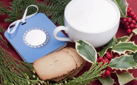 HD wallpaper of a cup of milk with cookies, surrounded by festive decorations including holly branches and red berries, making for a cozy and seasonal backdrop.