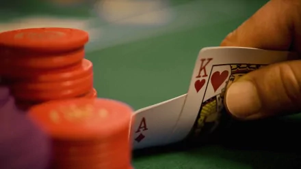 HD desktop wallpaper showing a close-up of a hand holding king and ace of hearts cards near red poker chips on a green felt poker table.