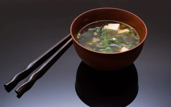 HD PC desktop wallpaper featuring a bowl of clear soup with tofu and green onions, accompanied by black chopsticks on a reflective dark surface.