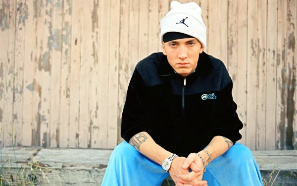 A high-definition desktop wallpaper featuring Eminem, sitting pensively against a weathered wooden backdrop, showcasing his iconic style and attitude in music culture.