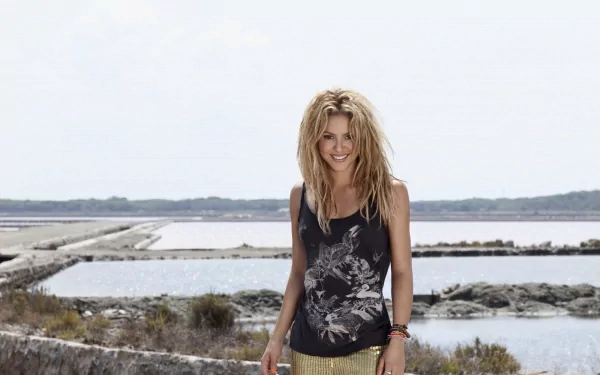 A vibrant HD desktop wallpaper featuring Shakira outdoors by a serene body of water, showcasing her fun, carefree style against a natural backdrop.