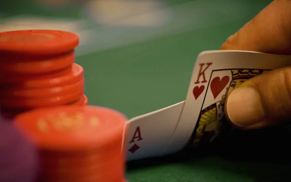 HD desktop wallpaper showing a close-up of a hand holding king and ace of hearts cards near red poker chips on a green felt poker table.