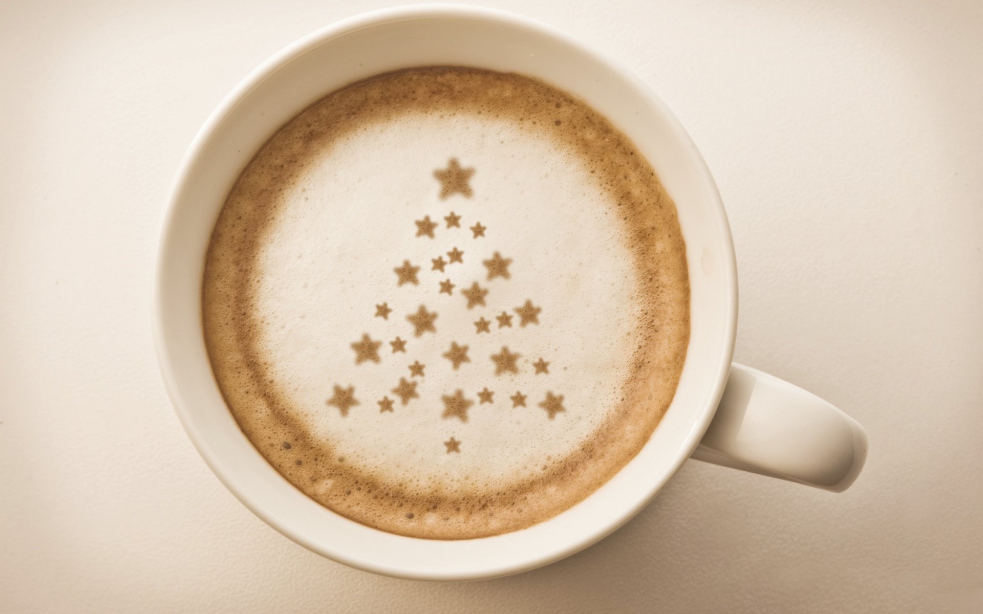 A top-down view of a coffee cup features a festive design of a Christmas tree made from star patterns on the frothy surface, serving as a vibrant HD desktop wallpaper.