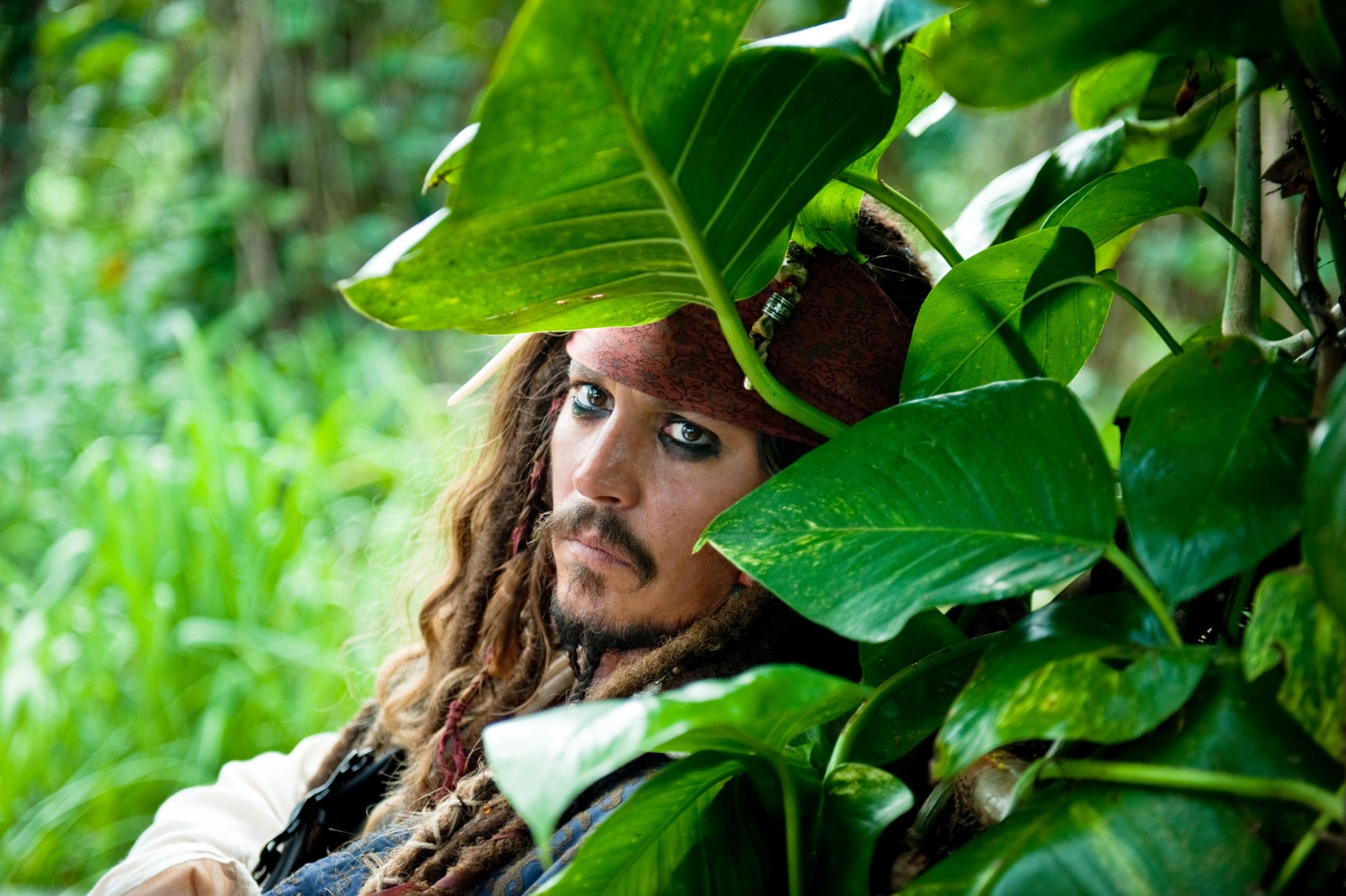 Jack Sparrow, portrayed by Johnny Depp, peeks through lush green leaves in a scene from Pirates of the Caribbean: On Stranger Tides, capturing the adventurous pirate spirit.