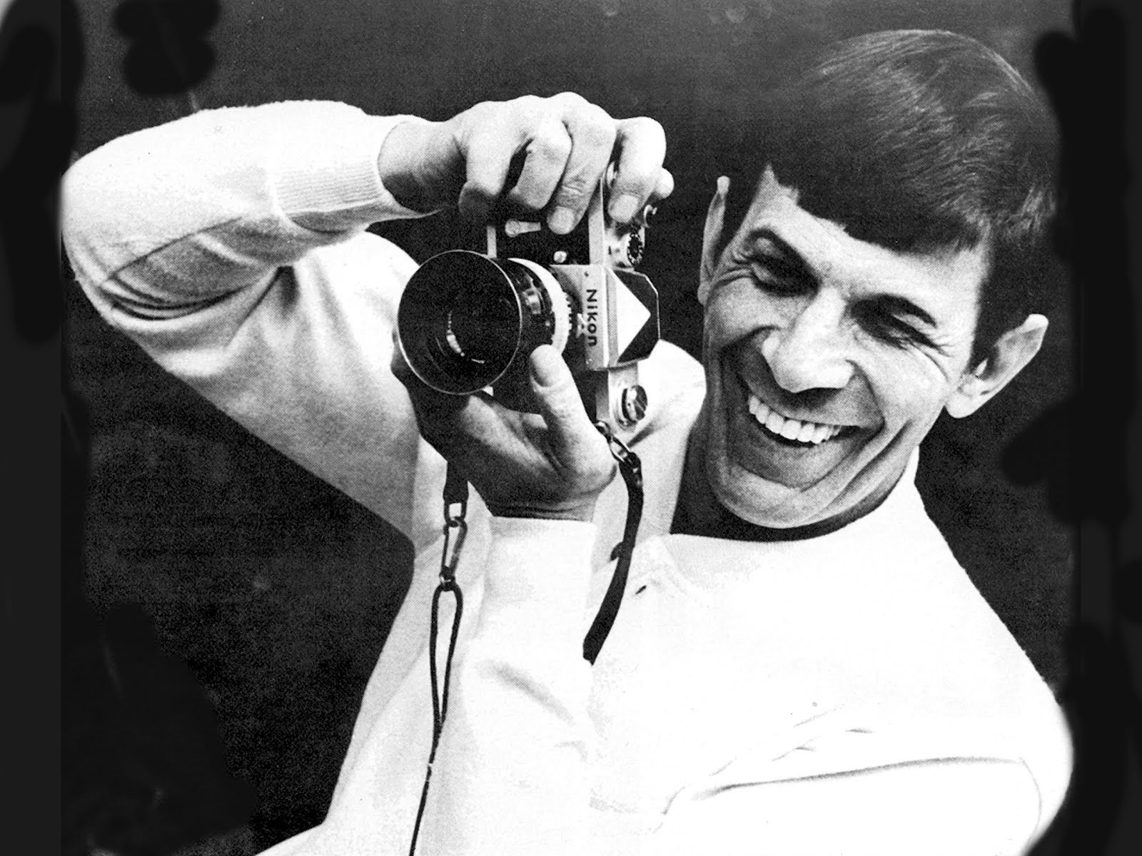 A black and white HD wallpaper featuring a cheerful man holding a camera, tagged as Leonard Nimoy.