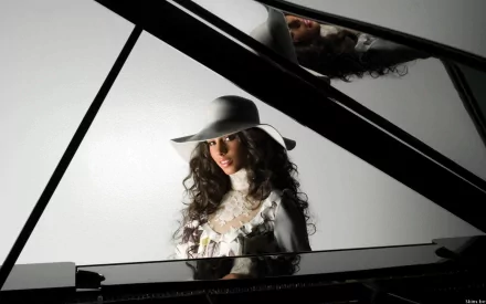 HD PC desktop wallpaper: studio portrait of a music artist in a wide-brimmed hat seated at a grand piano, reflective lid showing her face, moody, soulful vibe.