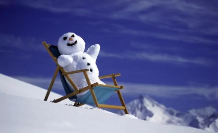 HD PC desktop wallpaper photography of a cheerful snowman reclining in a deck chair on a snowy slope with distant mountains and a deep blue sky.
