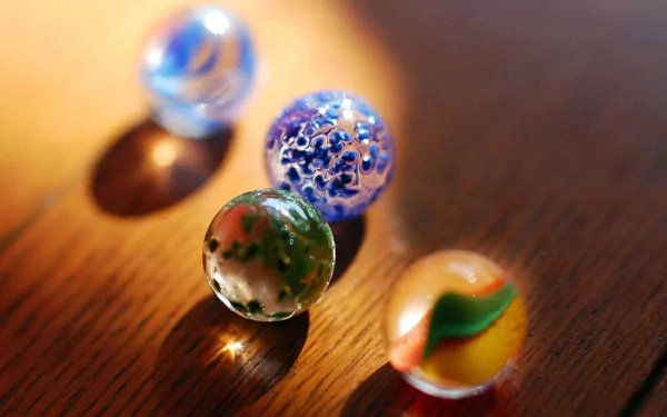 HD PC desktop wallpaper featuring an abstract close-up of four colorful glass balls on a wooden surface with soft lighting and shadows.