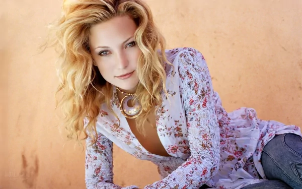 HD desktop wallpaper featuring celebrity Kate Hudson with wavy blonde hair, wearing a floral blouse against a warm, peach-toned background.