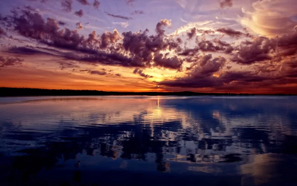 HD PC desktop wallpaper featuring a vibrant sunset over calm water, with dramatic clouds reflecting on the surface, showcasing the beauty of nature.