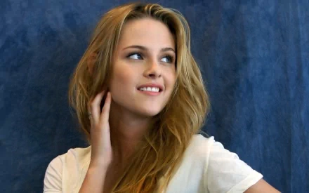 A blonde woman, tagged as actress and celebrity Kristen Stewart, smiles against a blue background in this HD desktop wallpaper.