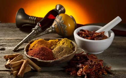 HD PC desktop wallpaper featuring a rustic wooden table with bowls of colorful ground herbs and spices, cinnamon sticks, dried chili peppers, and traditional grinding tools.