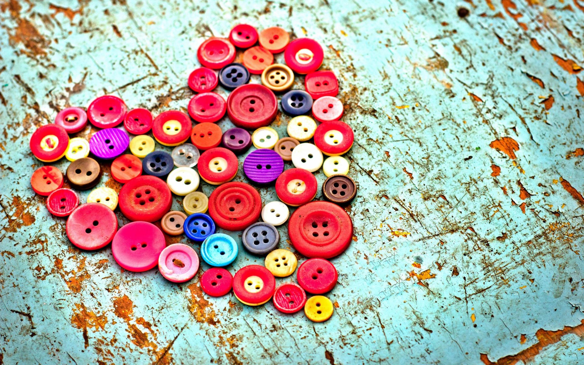 A vibrant heart composed of colorful buttons, set against a textured turquoise background, creates an artistic wallpaper for a desktop.