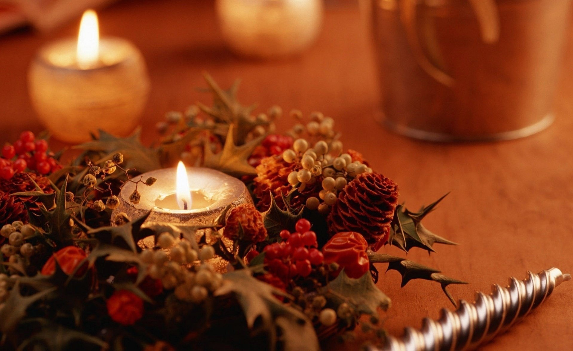 A beautifully arranged holiday scene featuring a lit candle surrounded by festive decorations, including berries and pinecones, creating a cozy Christmas atmosphere.