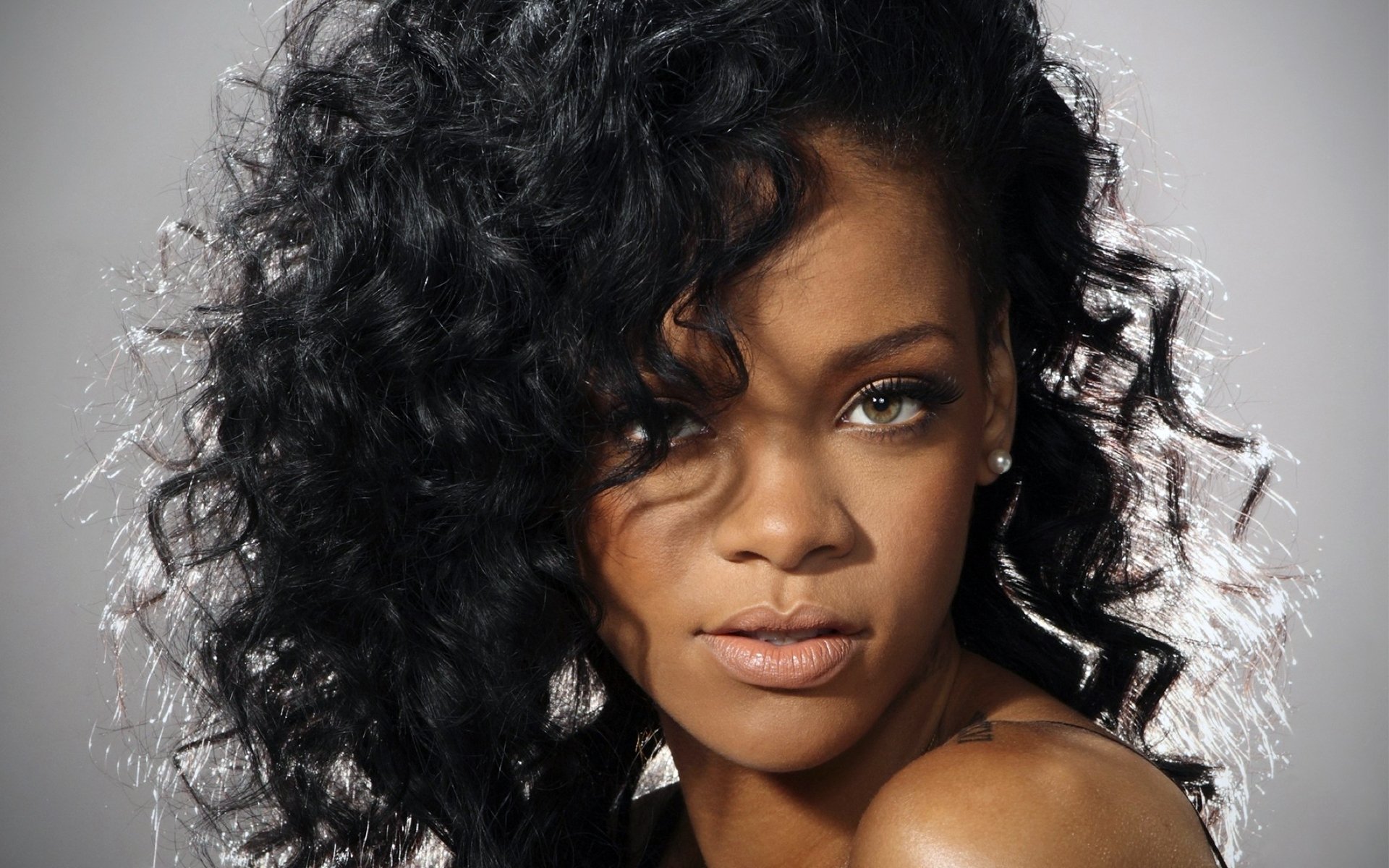 HD PC desktop wallpaper featuring a close-up of Rihanna with curly hair, highlighting her intense gaze and natural beauty in a music-themed portrait.