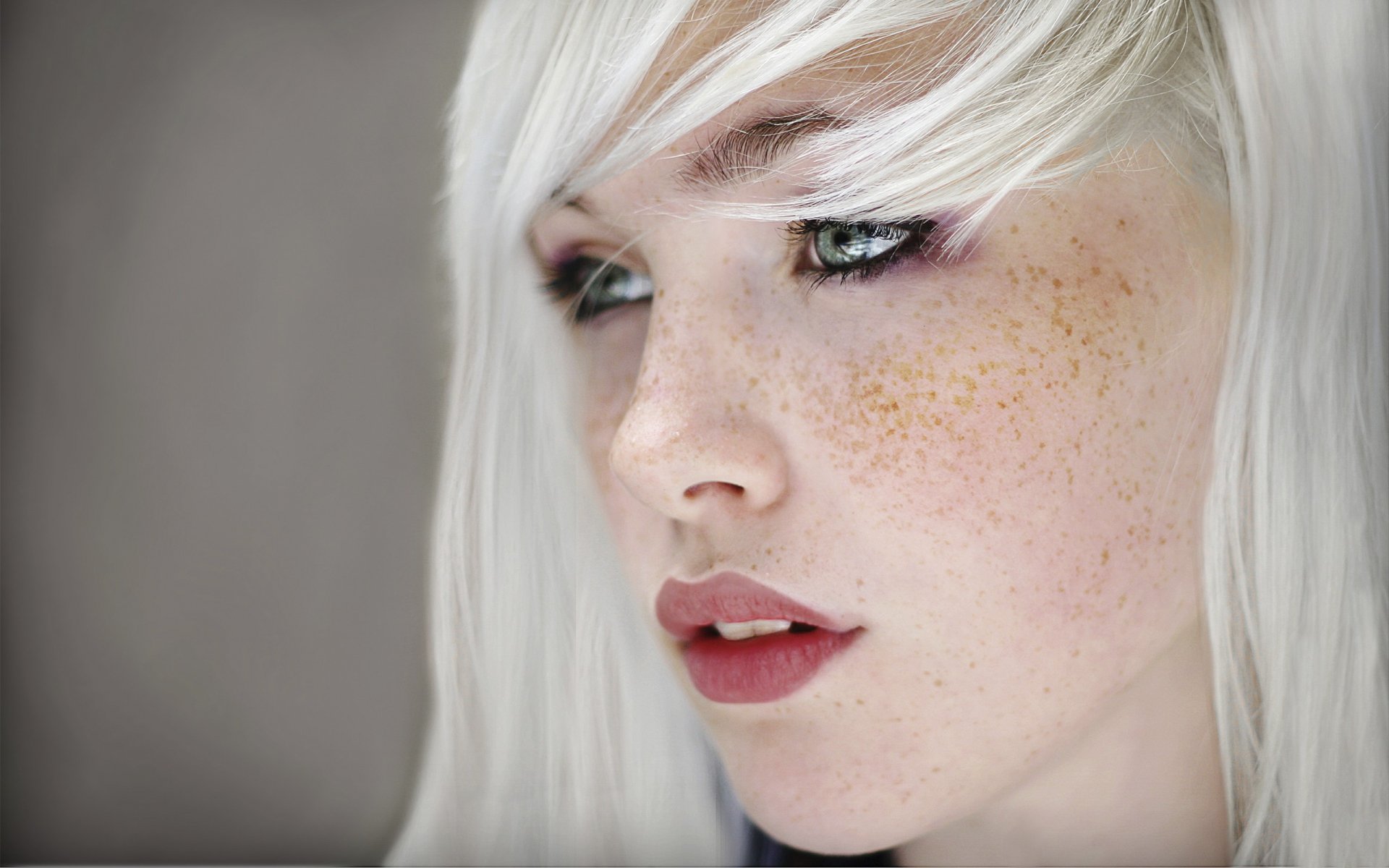 HD wallpaper featuring a close-up of a person with white hair, freckles, and a thoughtful expression.