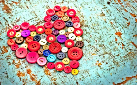 A vibrant heart composed of colorful buttons, set against a textured turquoise background, creates an artistic wallpaper for a desktop.
