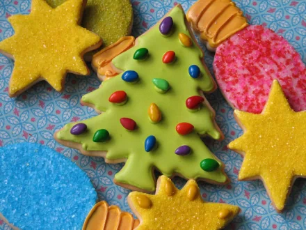 HD desktop wallpaper of colorful Christmas biscuits: a green Christmas-tree cookie topped with candy 'lights', surrounded by yellow star cookies and pink/blue sugar rounds.