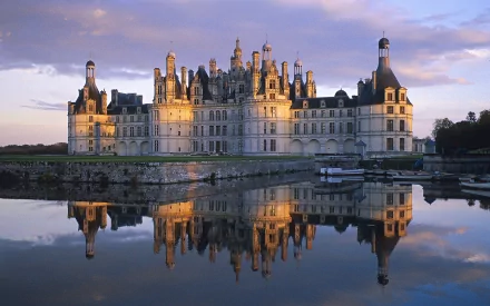 HD desktop wallpaper featuring the Château de Chambord in France, with the grand castle beautifully reflected in calm waters under a dramatic sky.
