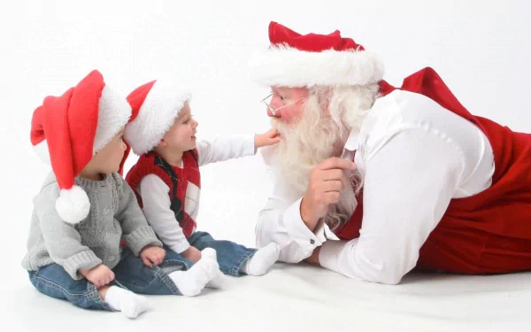 Two cheerful babies in Santa hats interact playfully with a jolly Santa Claus, embodying the joyful spirit of the holiday season in this delightful Christmas wallpaper.