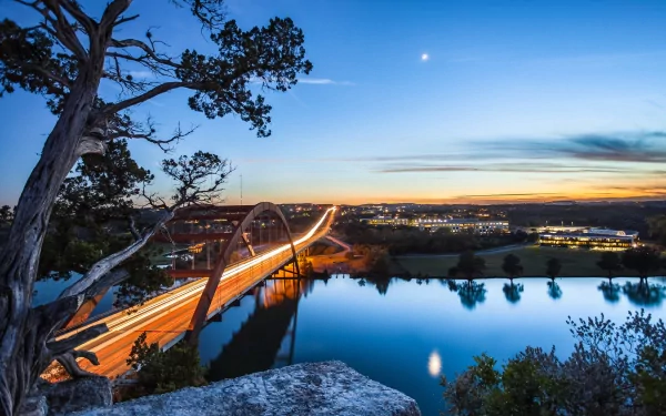 HD PC desktop wallpaper: Pennybacker Bridge, a man-made arched bridge in Austin, Texas, lit at dusk with traffic trails reflected in the river.