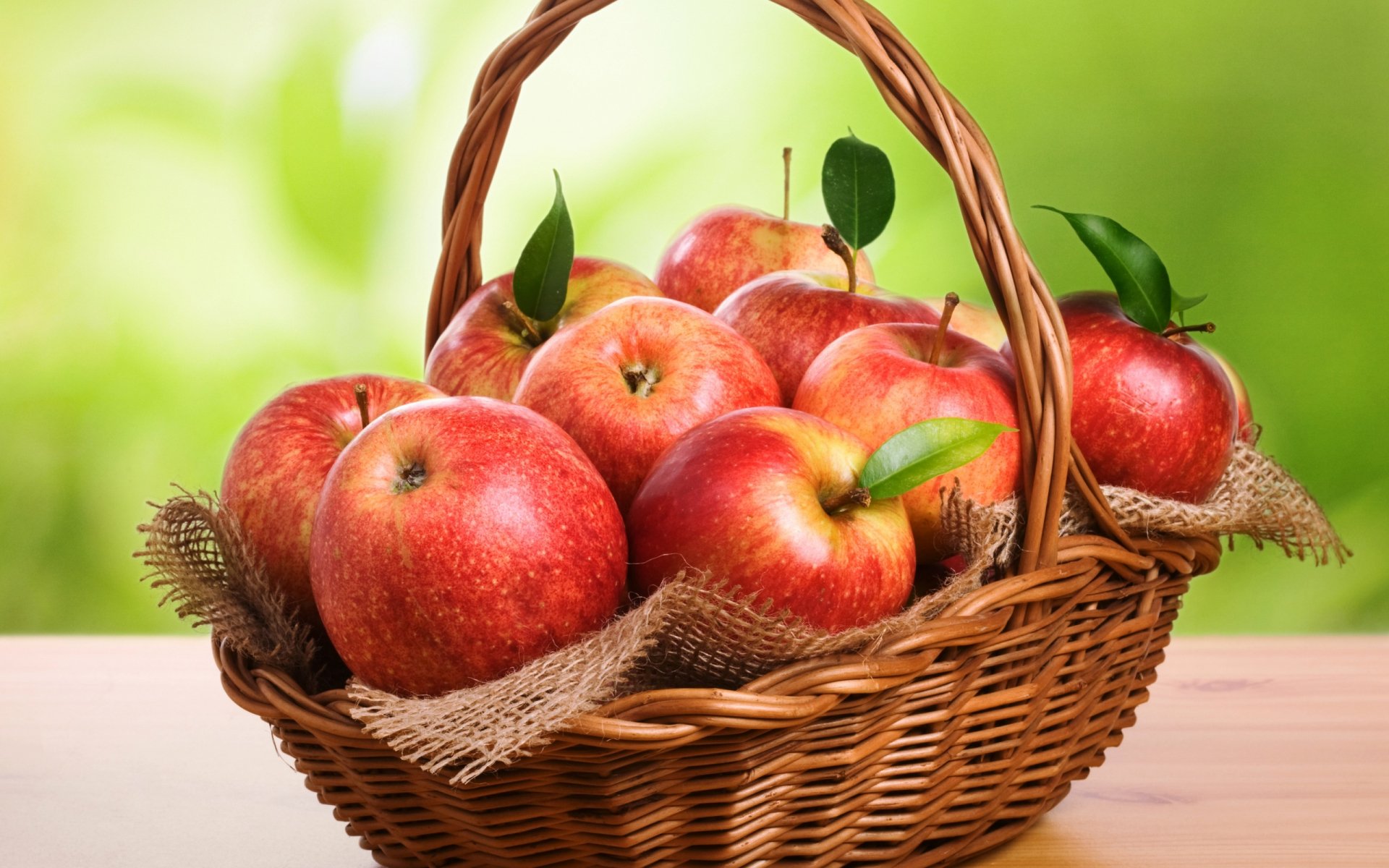 HD desktop wallpaper featuring a basket filled with fresh red apples against a soft green blurred background, highlighting food and apple themes.