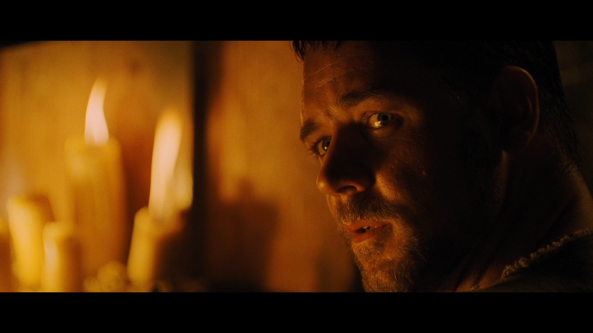 HD desktop wallpaper and background featuring a scene from the movie Gladiator, with a close-up of a determined man lit by flickering candles.