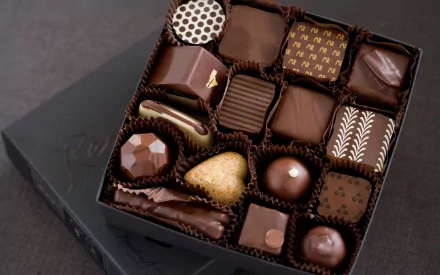 A high-definition desktop wallpaper featuring a variety of elegantly crafted chocolates arranged in a black box, showcasing different shapes and designs.