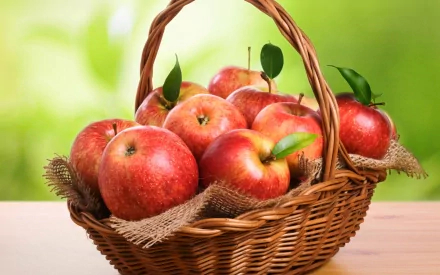 HD desktop wallpaper featuring a basket filled with fresh red apples against a soft green blurred background, highlighting food and apple themes.