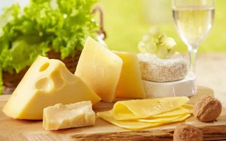 HD PC desktop wallpaper showcasing an assortment of cheeses, including Swiss, Brie, and sliced cheddar, accompanied by grapes, walnuts, and a glass of white wine.