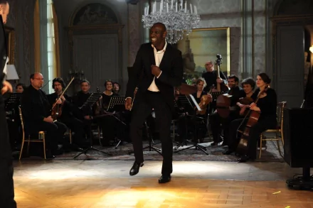 HD desktop wallpaper from Intouchables featuring a joyful man dancing in front of an orchestra in an elegant room.