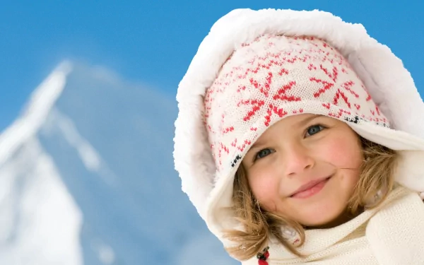 4K Ultra HD photography of a smiling child wearing a winter hat with a snowy mountain blurred in the background, captured as a vibrant PC desktop wallpaper.