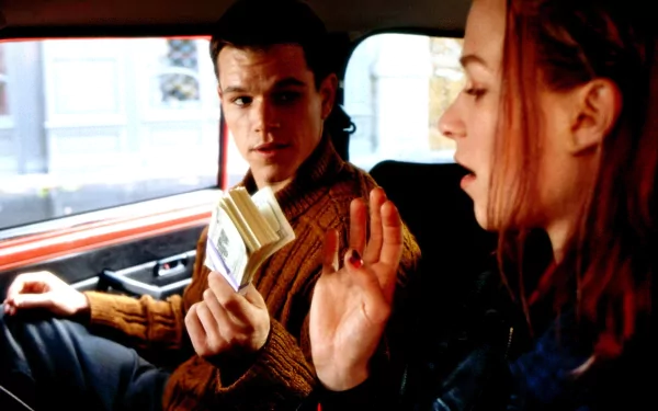 HD wallpaper from The Bourne Identity featuring two characters in a tense conversation inside a car.