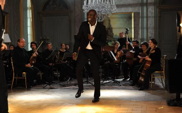 HD desktop wallpaper from Intouchables featuring a joyful man dancing in front of an orchestra in an elegant room.