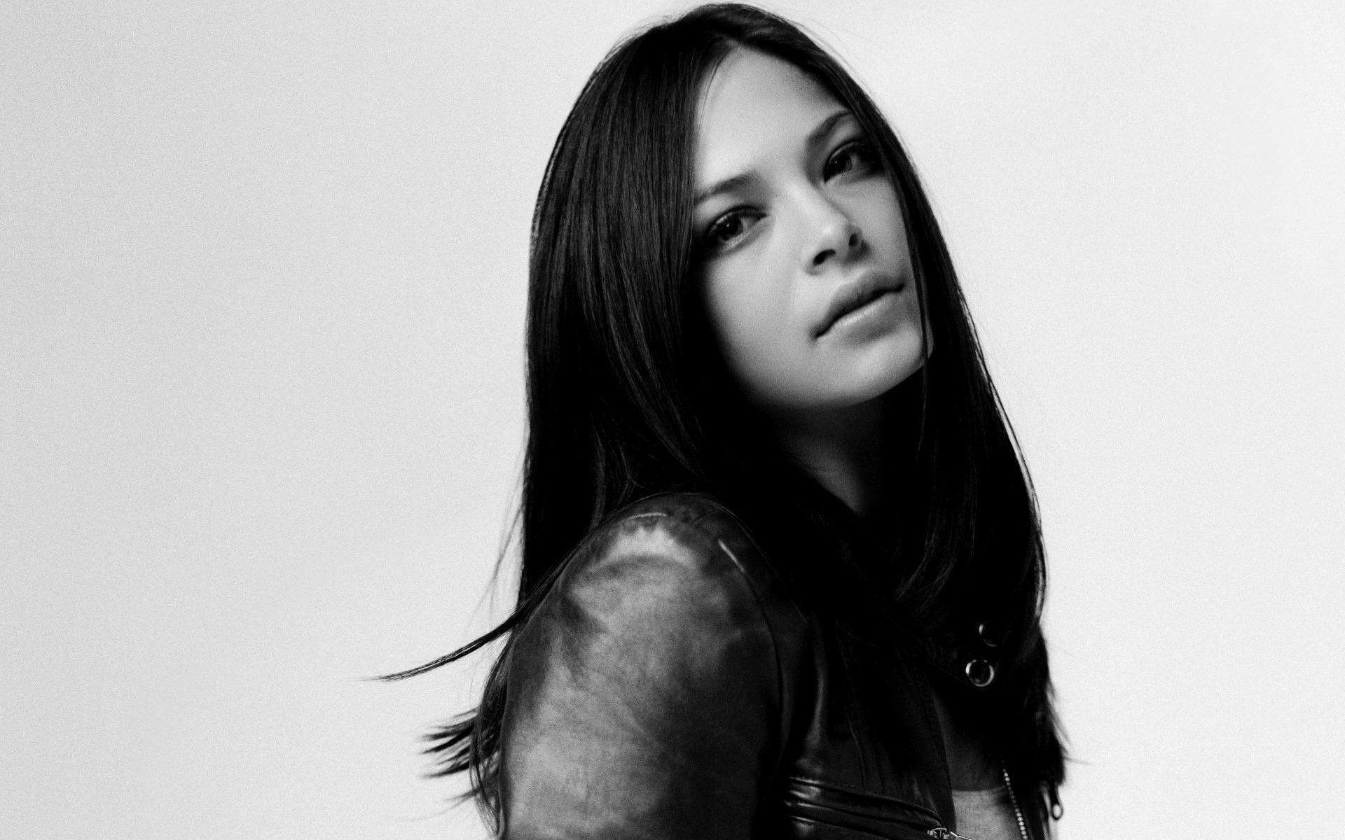 HD black-and-white desktop wallpaper featuring celebrity Kristin Kreuk with long dark hair and a leather jacket against a plain background.