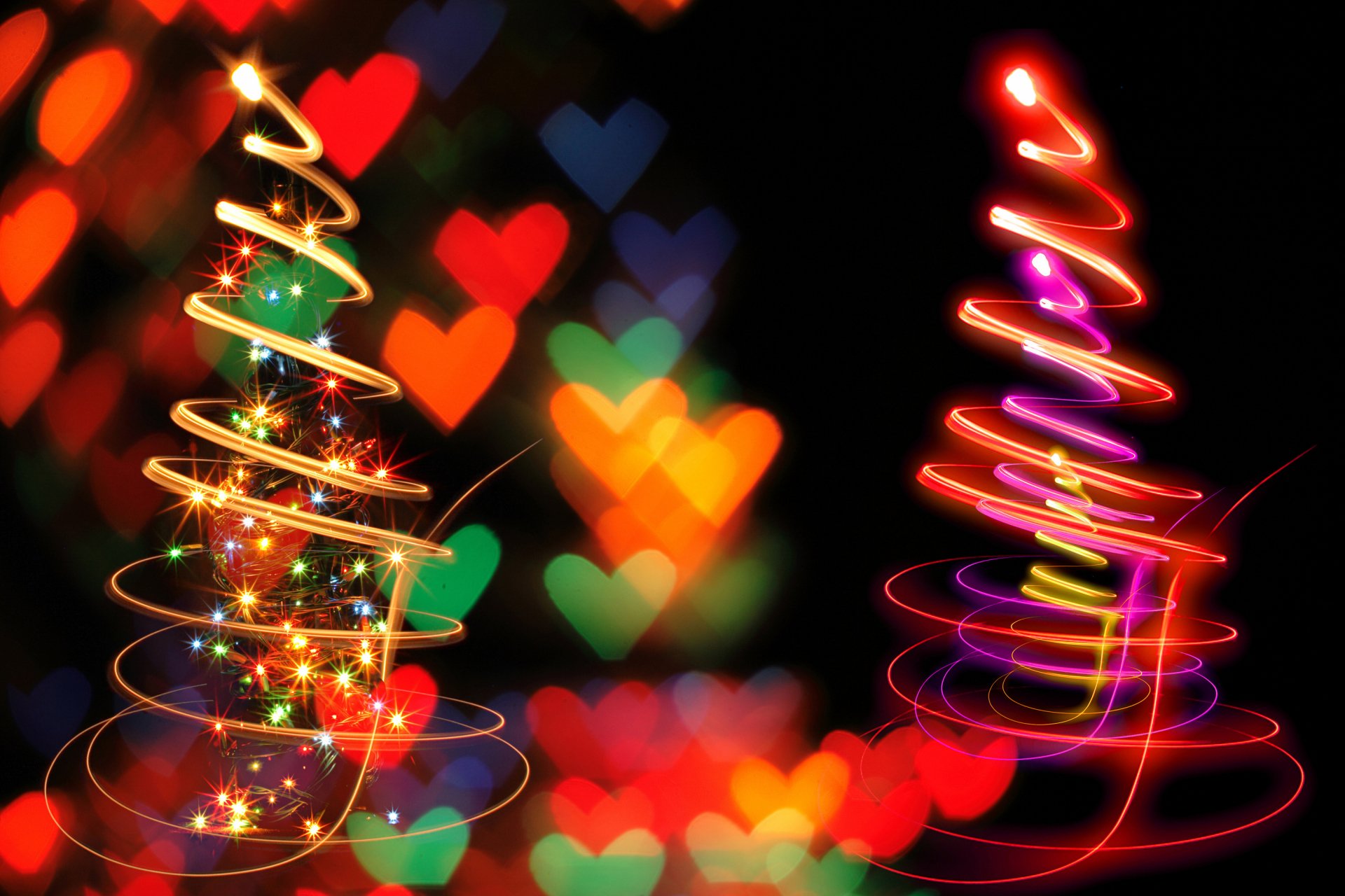 Colorful, glowing Christmas trees with heart-shaped bokeh lights create a festive holiday scene, designed as a vibrant HD PC desktop wallpaper and background.