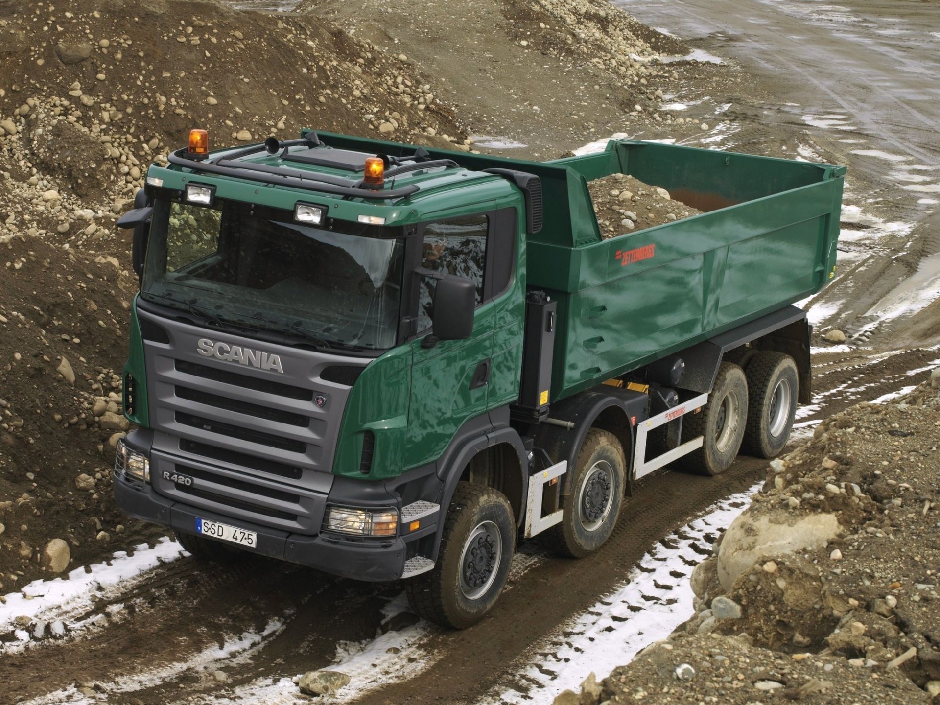HD desktop wallpaper of a green Scania dump truck carrying soil on a rugged construction site, showcasing the vehicle's robust design and functionality.