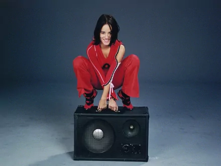 HD PC desktop wallpaper featuring music artist Alizée crouching on a large speaker, dressed in a red outfit against a dark background.