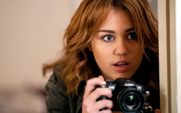 A captivating HD desktop wallpaper featuring Miley Cyrus, focused intently while holding a camera, exuding curiosity and charm in a candid moment.