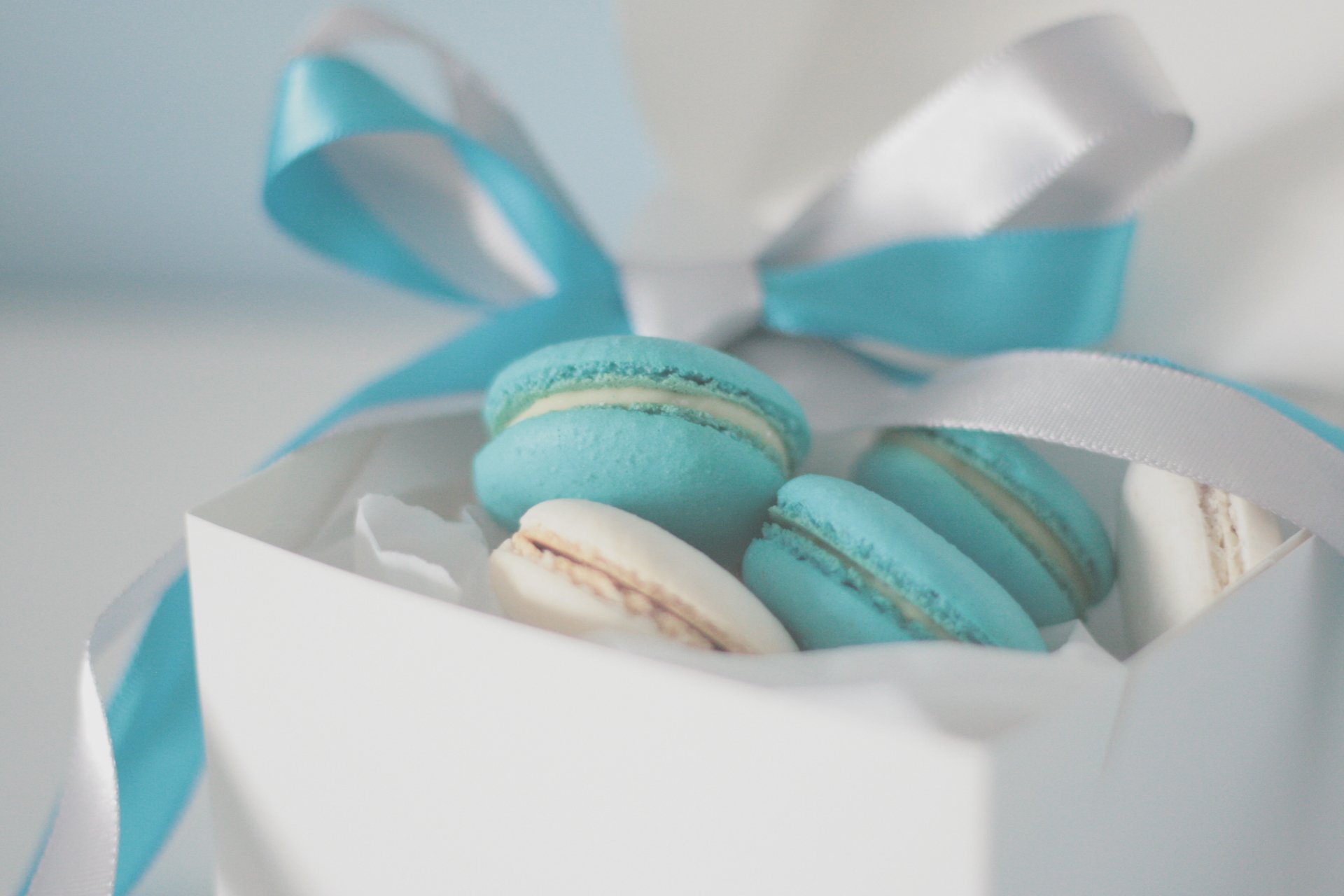 A close-up of blue and white macarons inside a white gift box with blue and white ribbons, captured in crisp 4K Ultra HD.