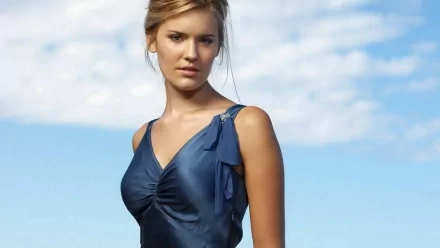 Maggie Grace poses elegantly in a blue dress against a clear sky, featured as an HD desktop wallpaper and background.