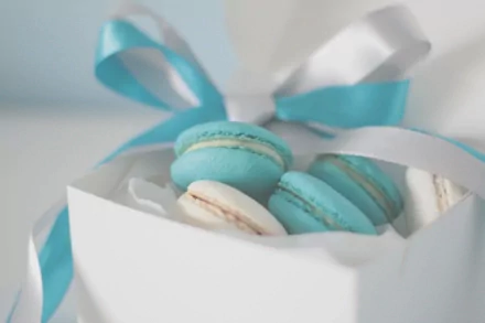A close-up of blue and white macarons inside a white gift box with blue and white ribbons, captured in crisp 4K Ultra HD.