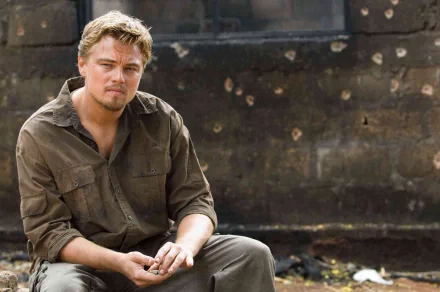 HD wallpaper featuring Leonardo DiCaprio from 'Blood Diamond', sitting pensively against a bullet-ridden backdrop.