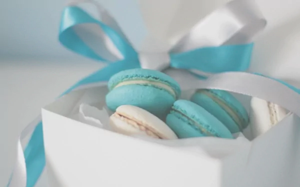 A close-up of blue and white macarons inside a white gift box with blue and white ribbons, captured in crisp 4K Ultra HD.